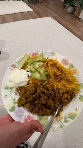 Customer's plated meal featuring cooked Halal Veal Cubes with yellow rice, sliced cucumbers, and a white sauce.
