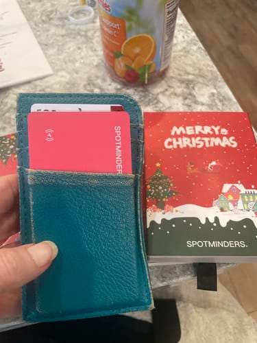 Customer holding a teal wallet with the red SPOTMINDERS Tracking Card inside, next to its festive Christmas packaging.