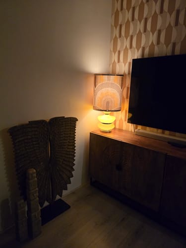 Klant toont de HKliving lampenkap met motief, verlicht op een gele voet in een woonkamer.