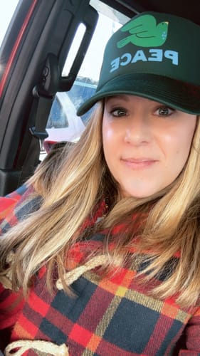 Reviewer wearing the green House of Peace Dove Trucker hat while sitting in a car.