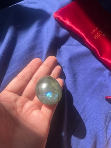 Customer holding a smooth, iridescent Monthly Crystal in their palm, with a red pouch in the background.
