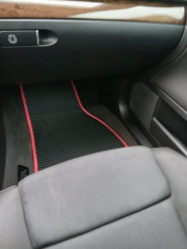 Recenzent pokazuje dopasowany czarny dywanik samochodowy z czerwonym obszyciem na podłodze po stronie pasażera.