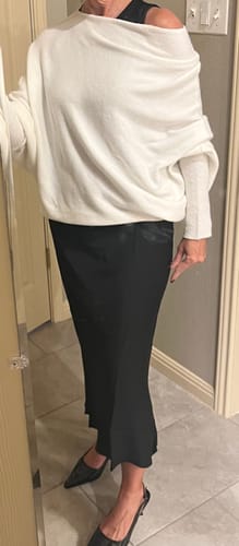 Reviewer wearing the ivory Asymmetric Draped sweater styled off one shoulder with a long black skirt.