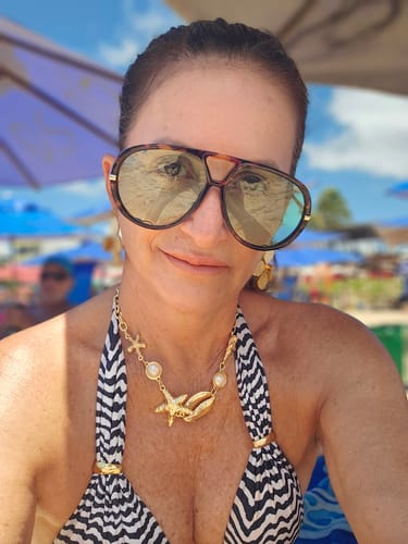 Avaliadora em close-up na praia, usando os Óculos Tropea com armação tartaruga e lentes esverdeadas.