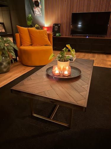 Klant toont de donkere Dutchbone Class Salontafel met visgraatblad in een sfeervolle woonkamer.