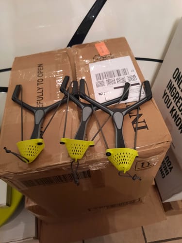 Recensent toont drie SLIK CATAPULTS V2 met felgele pouches op een doos.