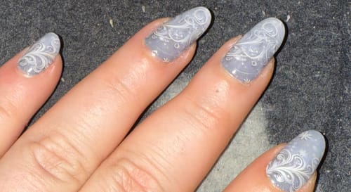 Nahaufnahme der Hand einer Person mit den eisgrauen Steel Blue Pearls Nagelfolien und filigranem Muster.