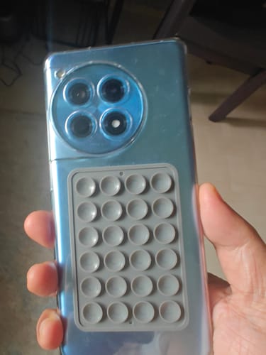 Customer holding a blue smartphone with the grey StickyPod suction mount attached to the back.