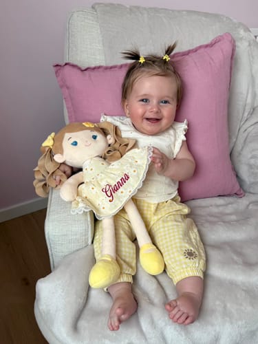Customer's smiling baby holds the yellow Personalized Daisy Girl doll, showing the custom 'Gianna' embroidery.
