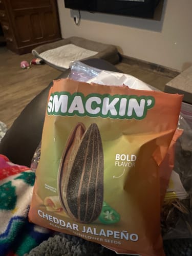 Customer's open bag of Smackin' Cheddar Jalapeño sunflower seeds resting on a couch in a living room.