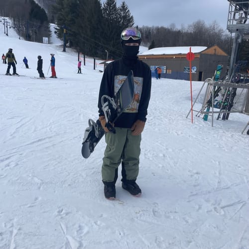 Reviewer wearing the army green baggy snow pants while holding a snowboard on a snowy slope.