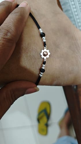 Close-up of a customer holding the Dual Tone Graceful Floral Anklet against their ankle, showing the silver flower charm and beads.