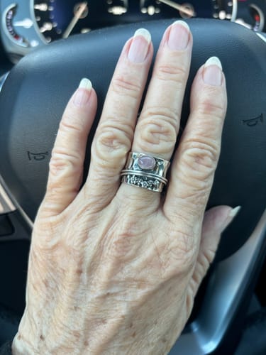 Reviewer's hand wearing the wide silver Rose Quartz spinner ring with a floral design.