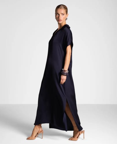 Reviewer wearing the long, navy Cleo Satin Kaftan Dress with a side split.