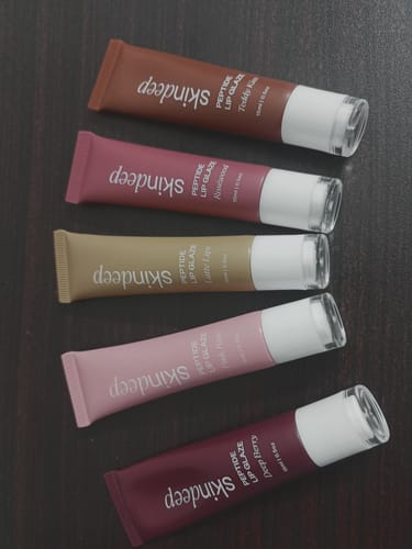 Reviewer's collection of five Peptide Lip Glaze tubes in different shades laid out on a dark surface.