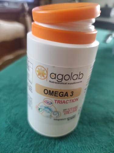 Recensore mostra il flacone bianco di Omega 3 Triaction di agolab con tappo arancione, posato su un tavolo.