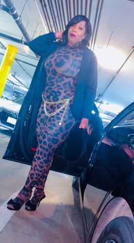Reviewer holding the black Faux Fur Plush Mini Bag while wearing a leopard print outfit in a garage.