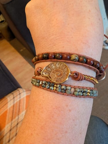 A reviewer's wrist wearing the beautiful wrap bracelet, showing the central ammonite fossil and multi-colored beaded strands.