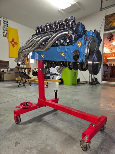 Customer's shiny Exhaust Header installed on a blue V8 engine mounted on a red engine stand in a garage.