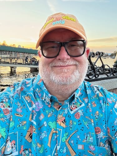 Reviewer smiling in the bright blue 'Lester’s Possum Park' shirt outdoors at sunset.