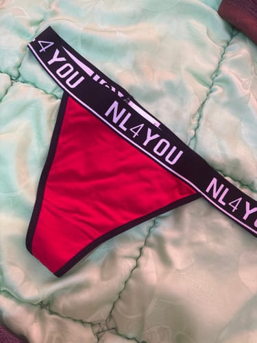 Customer's red and black thong underwear with a branded waistband, laid flat on a green comforter.