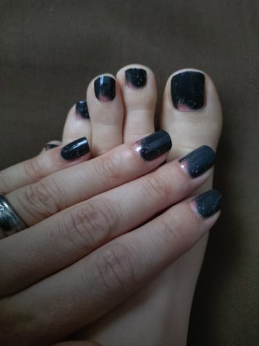 Kundin zeigt ihre Finger- und Fußnägel mit dem dunklen, glitzernden Nageldesign Starry Horizon.