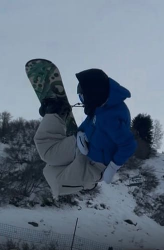 Reviewer in mid-air on a snowboard, wearing the light gray baggy snow pants with a blue jacket.