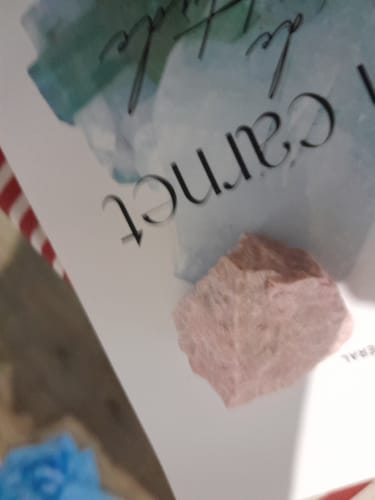 Gros plan sur la pierre Thulite brute et rose d'un client, posée sur un carnet.