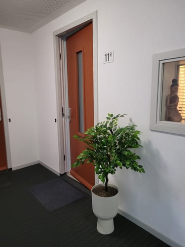 Recensent toont de witte Elho Vibes Fold Coupe bloempot met een kunstplant in een hal.