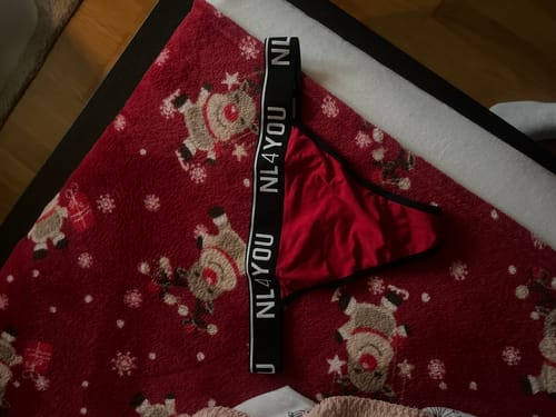 Customer's red Christmas thong with a black branded waistband, laid out on a festive reindeer blanket.
