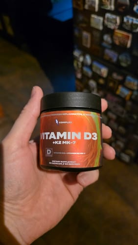 A customer's hand holding a black jar of Complex Vitamin D3+K2 MK-7 supplements.