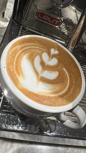A customer's latte made with Golden Cup Blend, showing detailed rosetta art in a white cup on an espresso machine.