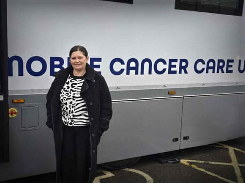 Reviewer wearing the Zebra Animal Knit Jumper under a black coat in front of a mobile cancer care unit.