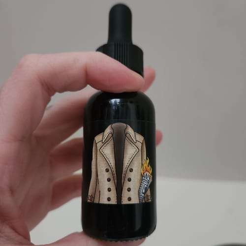 Customer holding a dark dropper bottle of Assbutt beard oil with a trench coat label.