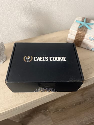 Customer's closed black box for Cael's Cookie, with the brand logo printed on top, sitting on a table.