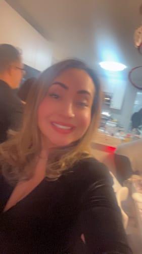 Close-up of a reviewer smiling while wearing the black Aless V Neck Velvet Mini Dress indoors.