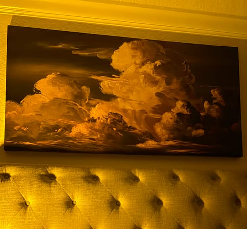 Customer's large Tailored Boost cloudscape artwork hanging above a tufted headboard under warm lighting.