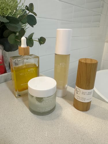 Reviewer's Radiance Body Oil in a square glass bottle, displayed on a bathroom counter with other skincare products.