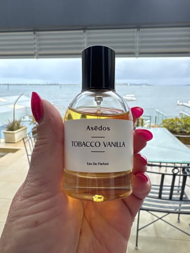 Reviewer holding the clear bottle of TOBACCO VANILLA EAU DE PARFUM outdoors on a patio.