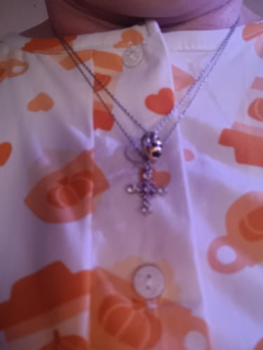 Close-up of a customer wearing the silver Adopt a Bee® Necklace layered with a second necklace against a patterned shirt.