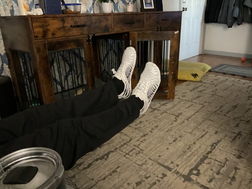 Customer relaxing on the floor with their feet up, wearing the white and black Lorax Pro barefoot shoes.