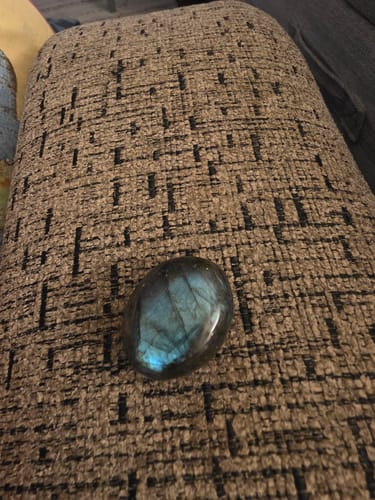 Customer's polished Labradorite crystal showing brilliant blue colors on a textured couch.
