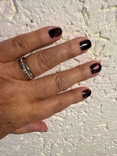 Hand einer Kundin mit einer Maniküre mit den dunklen, glänzenden Amber Fire (Chrome) Nagelfolien.