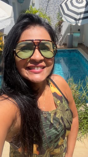Cliente sorrindo ao usar os óculos Tropea, mostrando a armação tartaruga e as lentes verdes em um dia ensolarado na piscina.
