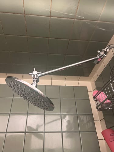 Customer's adjustable shower arm and rain shower head installed in a shower with green tiles.