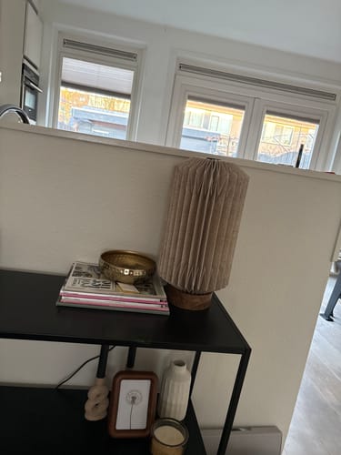 Recensent toont de by fonQ Linen Tafellamp met zijn unieke geplooide kap op een zwarte consoletafel.