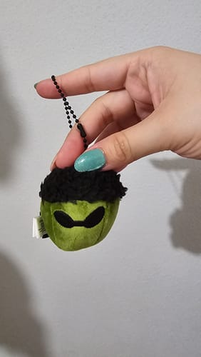 Customer holding the small, plush green Acorn Charm with a black fuzzy top and sunglasses.