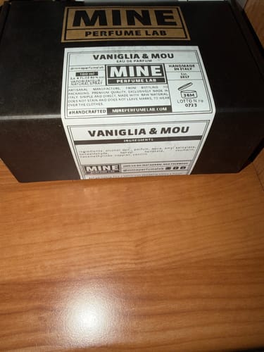 Recensore mostra la scatola nera del profumo VANIGLIA & MOU su un tavolo.