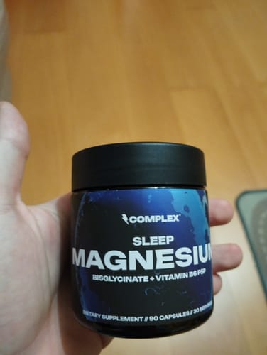 Customer holding a black jar of Complex Sleep Magnesium supplement against a wooden floor.