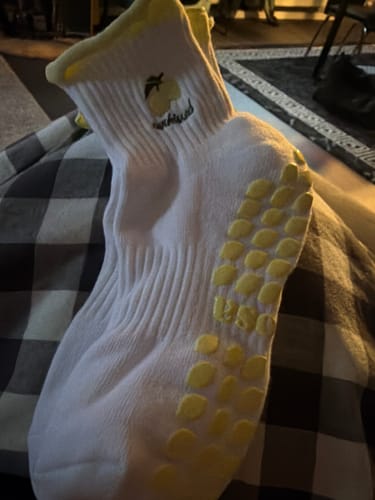 Close-up of a reviewer's thick white Sunkissed socks with yellow cuffs and lemon-shaped grips on the sole.